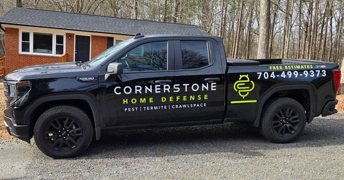 cornerstone-home-defense-pest-termite-crawlspace-south-carolina Black Cornerstone Home Defense truck with lime green branding and phone number parked in front of a brick home.