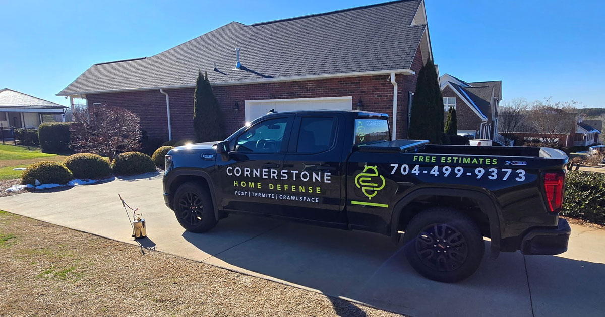 cornerstone-home-defense-quarterly-pest-control-services-north-carolina Black Cornerstone Home Defense truck with lime green branding and phone number parked in front of a brick home.
