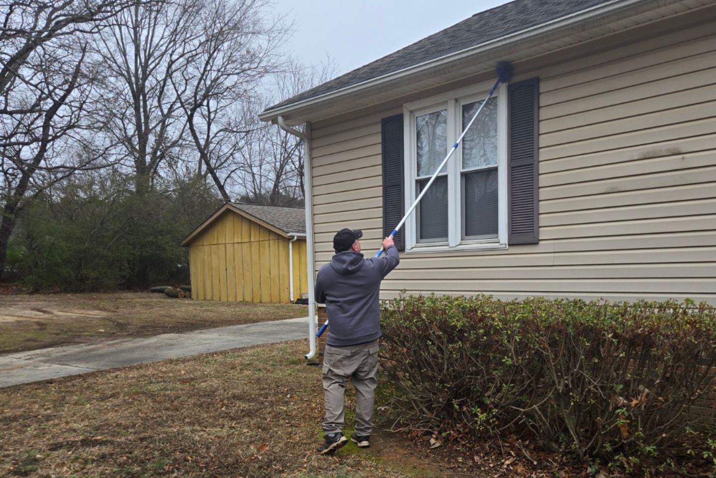 Cornerstone Home Defense technician removing webs and wasps nest from under roof eaves with long webduster.